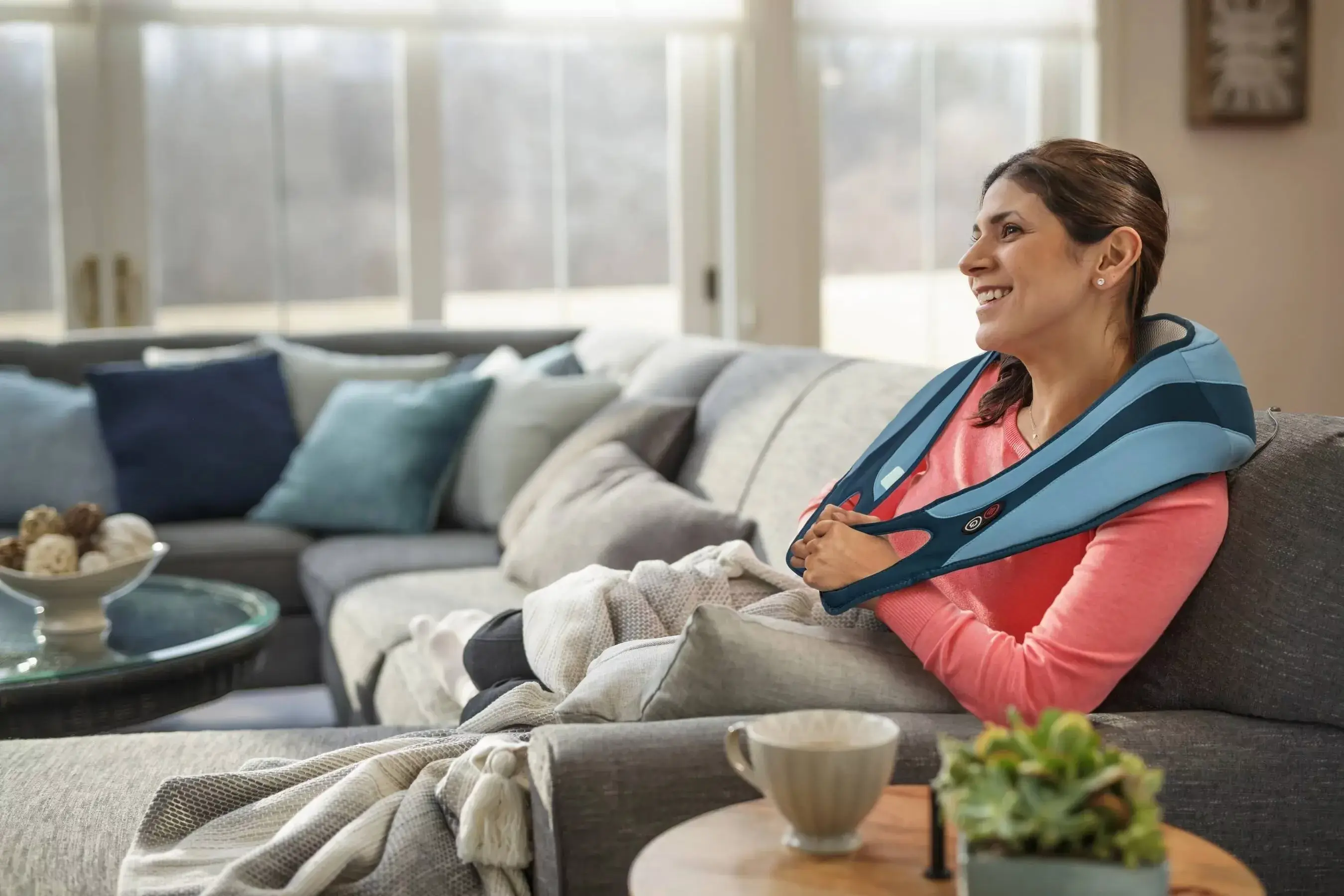 A woman uses a massager while sitting on the couch to help relieve pain.